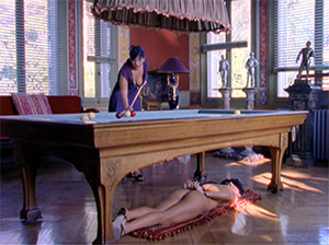 Isabella blindfolded under the pool table as Dahlia shoots
